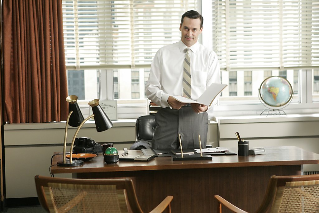 Don Draper standing at his desk in a 1960s advertising office